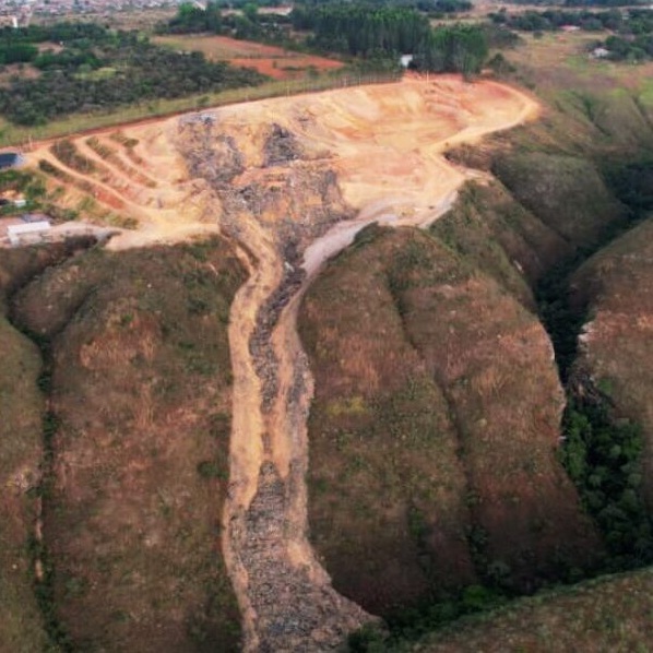 Vista aérea de um desabamento em um lixão, mostrando uma pilha de lixo escorregando pela encosta em uma área com vegetação ao fundo.