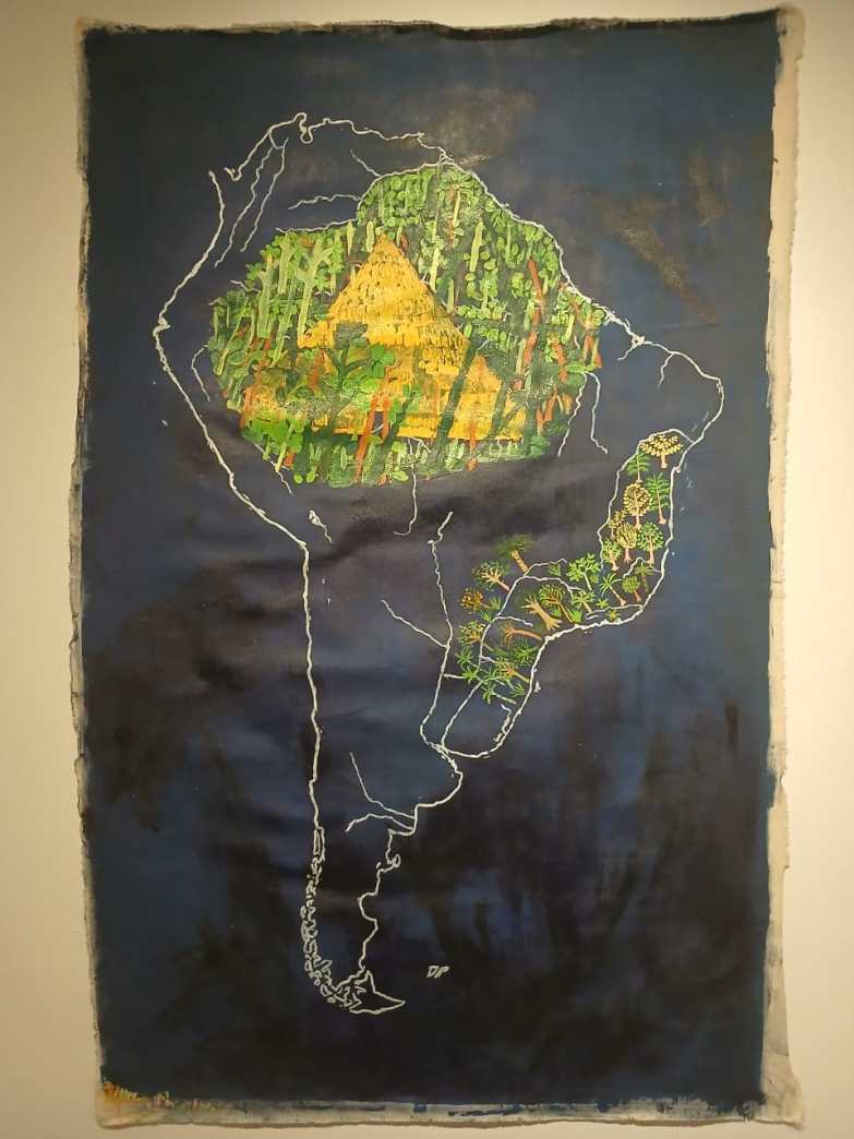 Arte em papel representando o mapa da América do Sul, com áreas da Amazônia detalhadas em cores vibrantes, incluindo elementos naturais como árvores e uma estrutura de forma triangular.