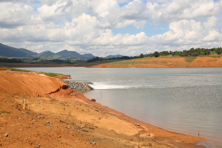 Vista do reservatório de água do Sistema Cantareira, com vegetação ao fundo e céu parcialmente nublado.