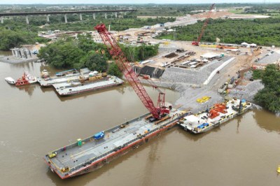 Vista aérea da obra de duplicação da ponte rodoferroviária sobre o Rio Tocantins, com um guindaste vermelho em destaque e áreas de construção ao fundo.