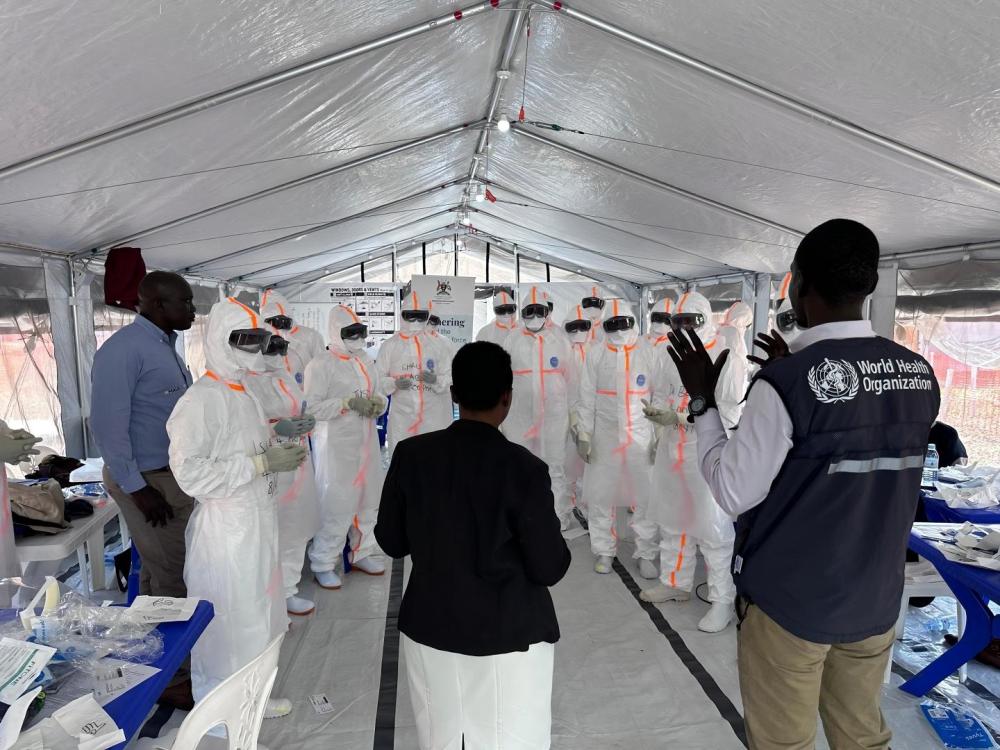 Equipe de saúde em trajes de proteção discutindo protocolo em um centro de tratamento de Ebola sob a supervisão da OMS.